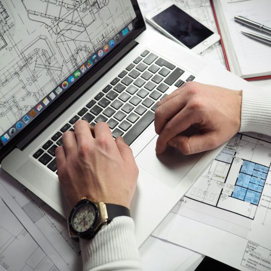 pexels-photo-110469-110469 Architect reviewing detailed floor plans and schematics on a laptop with a smartphone nearby.