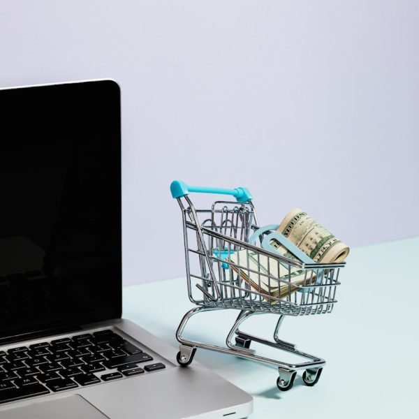pexels-photo-5632379-5632379 Mini shopping cart with rolled cash next to a laptop, representing online shopping.
